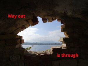 From a dark room, a view through a breach in the wall to a sunny seascape. On the background of the wall the inscription "Way out is through".